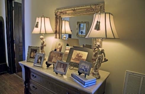 Victorian dresser with antique pictures and frames on top and two lamps with antique mirror hanging above