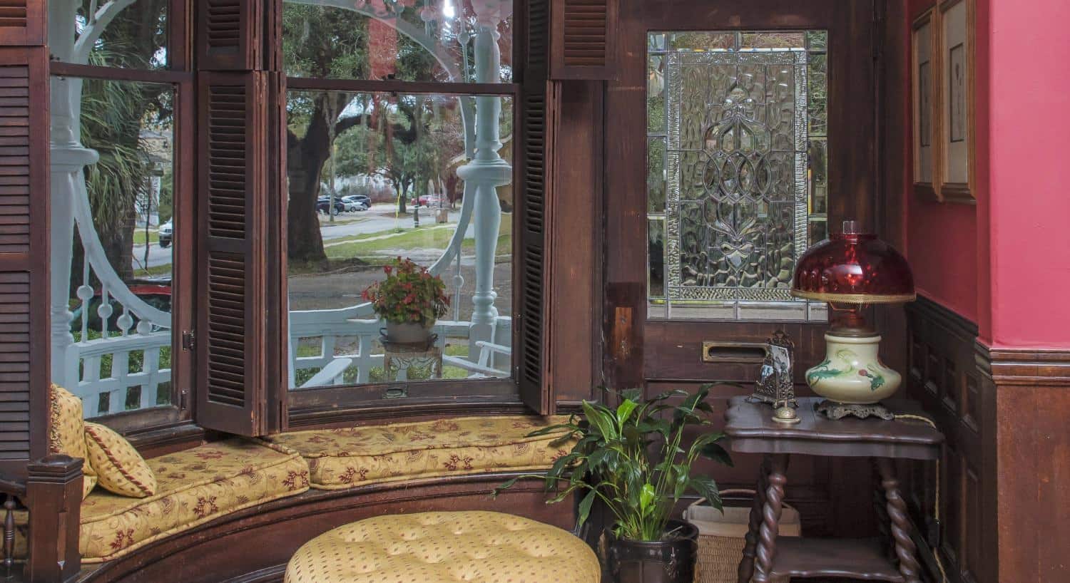Large picture window with dark brown wooden shutters and gold and burgundy floral upholstered cushions