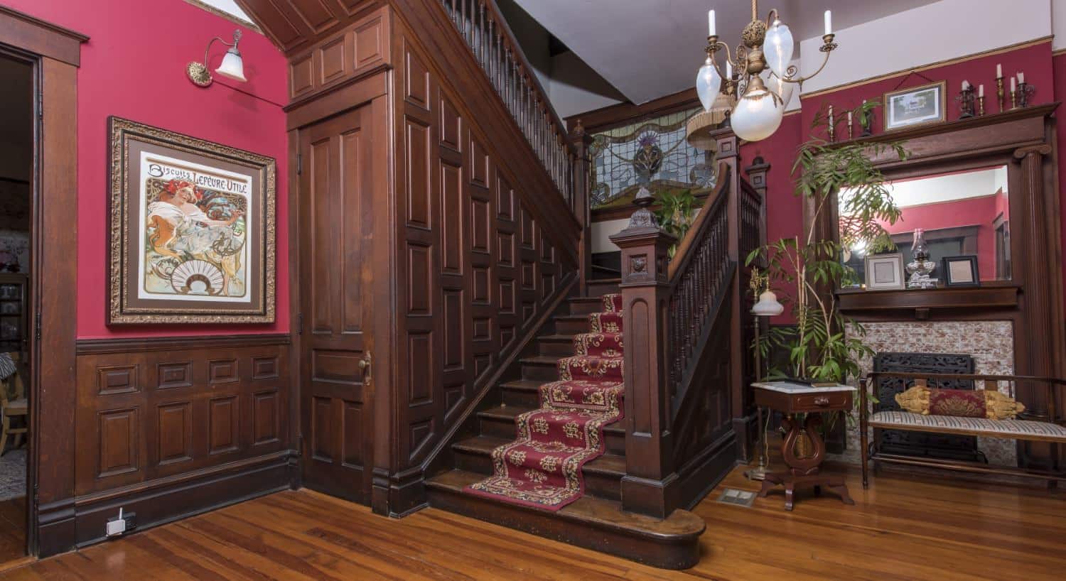 Large staircase with dark brown ornate wood railing and paneling with floral burgundy stair runner