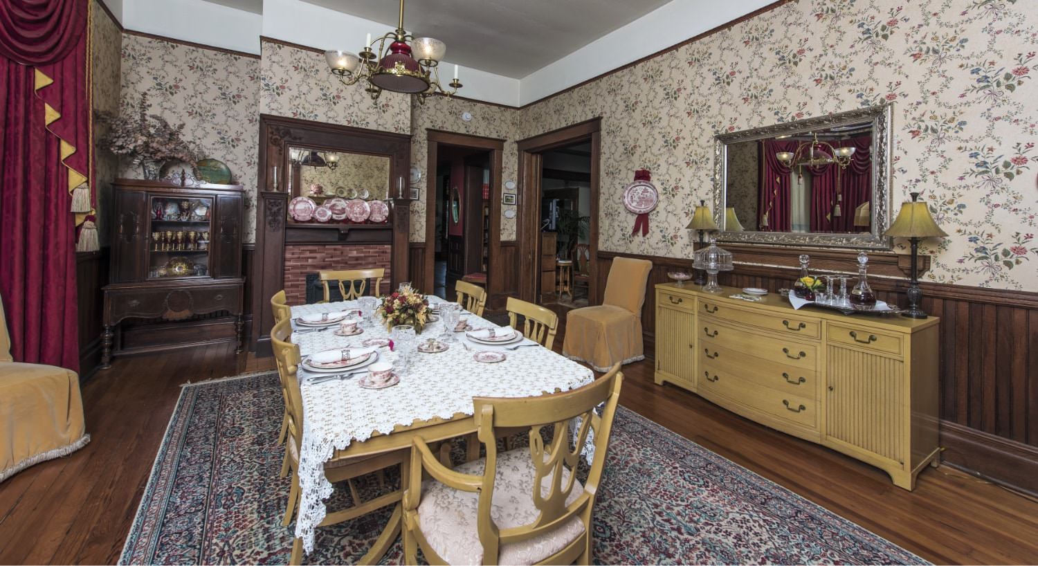 Dining room with light brown table, chairs, and buffet, dark brown hardwood floors, and floral wallpaper