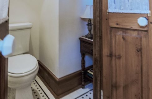View into bathroom with light tan walls, wooden trim, black and white tiled floor, and white toilet