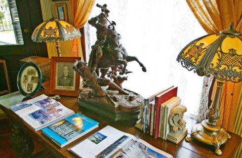 Old wooden table with books, old pictures and frames, antique lamps, and bronze miniture statue on top