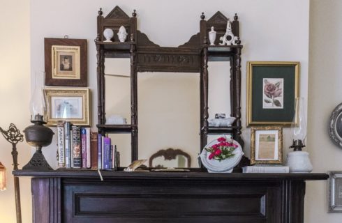 Dark wooden mantel with Victorian mirror, old kerosene lamps, and books
