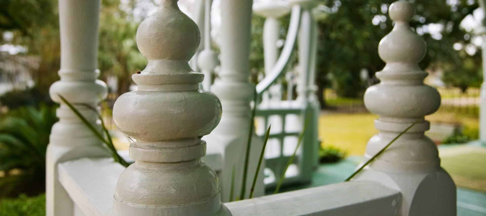Close up view of front porch pillars painted white with grass and plants in the background